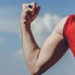 Close-up of a flexed arm in a red shirt against a clear blue sky, symbolizing strength and empowerment.